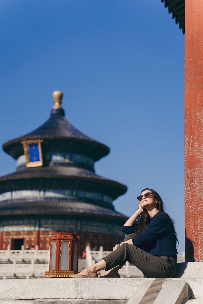 Mujer sentada mirando hacia el sol, y de fondo el templo del cielo en pekin