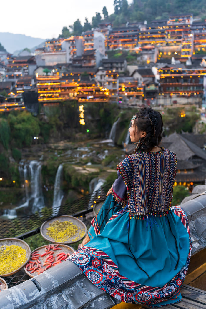 Mujer sentada al borde del techo de una casa mirando hacia la ciudad de lijiang en china